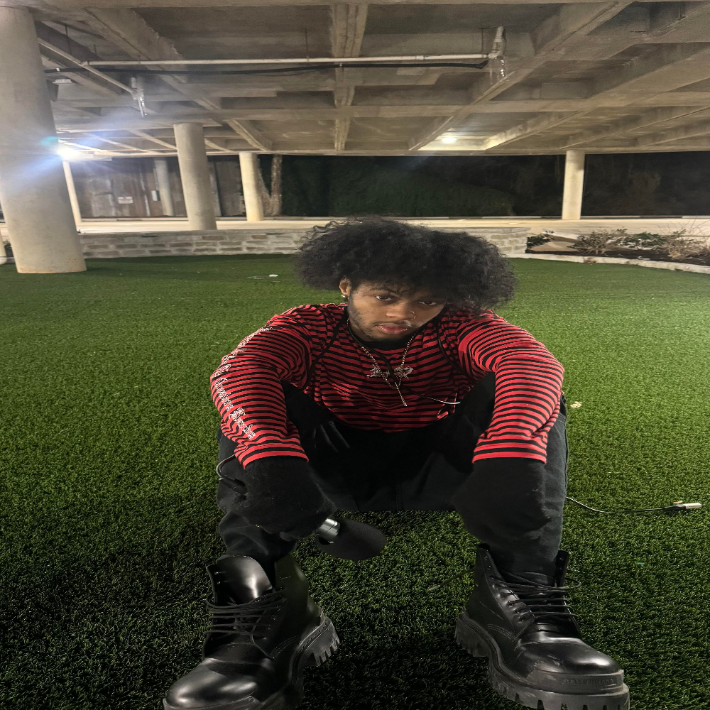Cxris wearing XXXTENTACION striped shirt and black Balenciagas holding on grass.